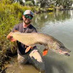 man in sunglasses holding a large fish that he caught in the river