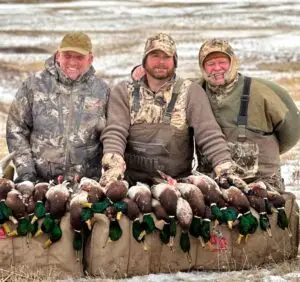 Three hunters smile as they pose with their harvest from a successful duck hunt.