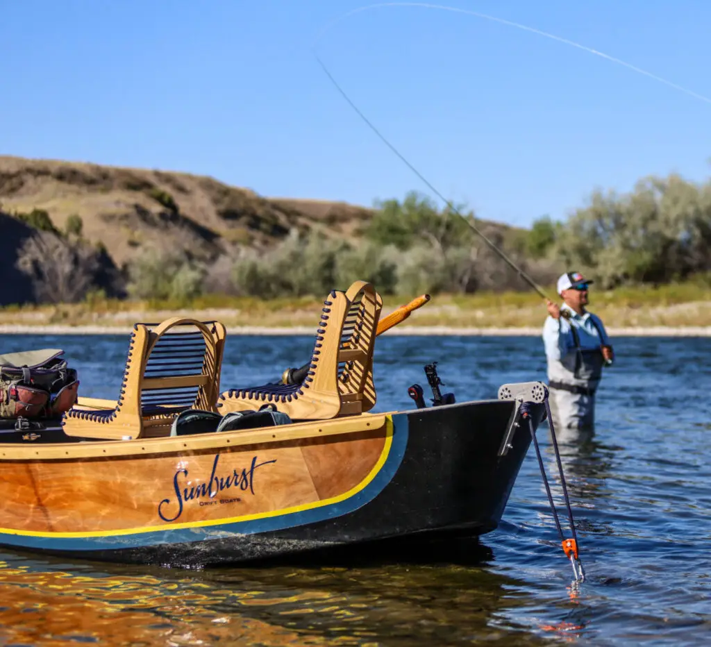 Drift boat anchored as a fly fisherman wades in the Big Horn River and casts his line.