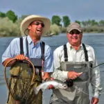 a man with a fishing net standing next to a man with a fly fishing rod