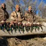 three men showing off the duck hunt harvest while wearing camouflage