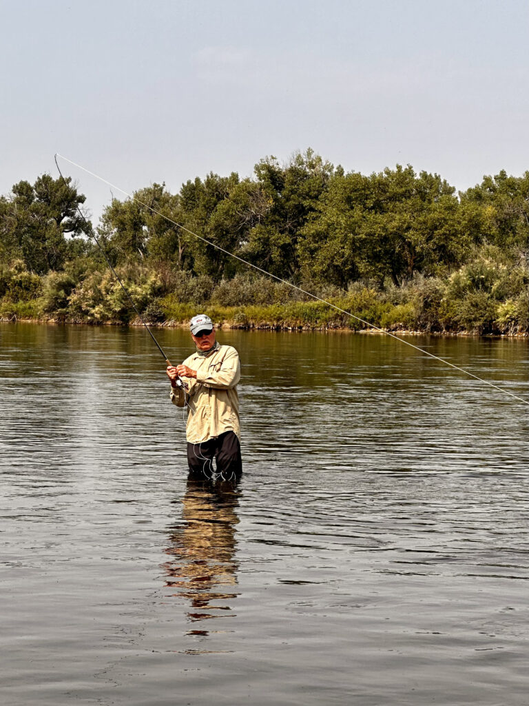 man standing in a river reeling in a fish on a fly rod